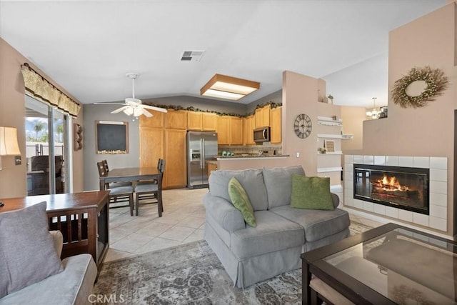 living area with vaulted ceiling, a ceiling fan, a tiled fireplace, and light tile patterned floors