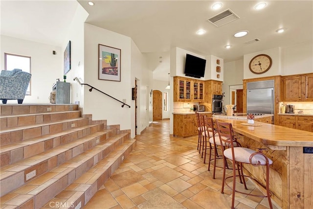 31024 Rabbit Springs Rd, Lucerne Valley, CA 92356 - kitchen featuring built in refrigerator, brown cabinetry, a kitchen bar, decorative backsplash, and light countertops