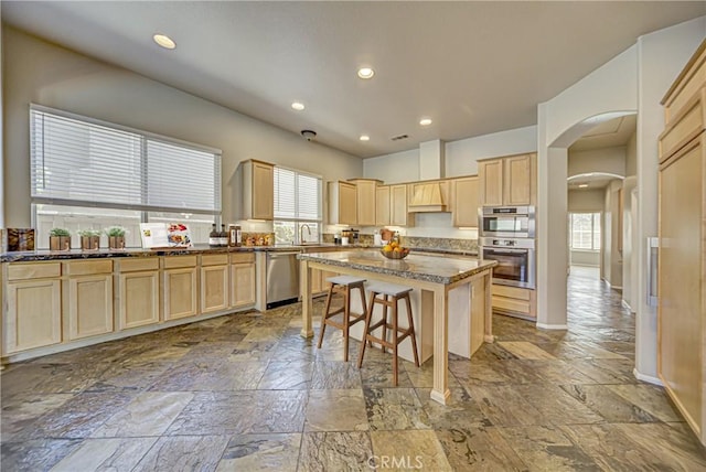 43922 Carentan Dr, Temecula, CA 92592 - kitchen with stainless steel appliances, stone tile floors, arched walkways, light brown cabinets, and a breakfast bar area