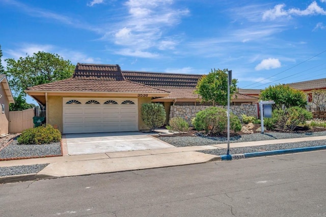 view of front of property with a tiled roof, a garage, stucco siding, driveway, and fence