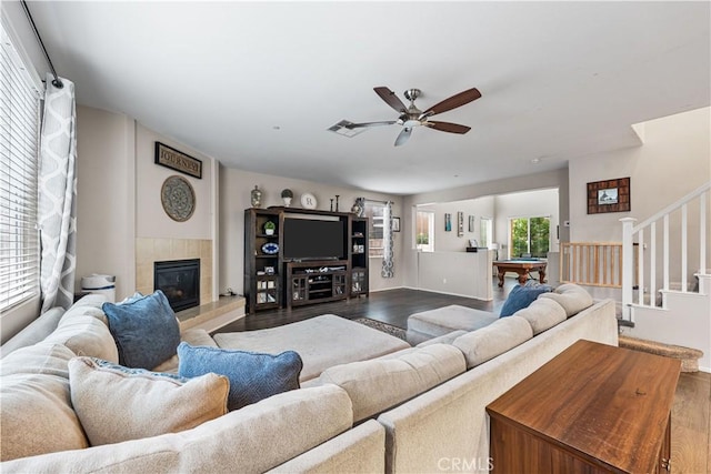 living area featuring wood finished floors, a ceiling fan, a tiled fireplace, stairway, and billiards