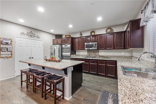 kitchen with appliances with stainless steel finishes, a sink, a center island, wood finished floors, and a breakfast bar area