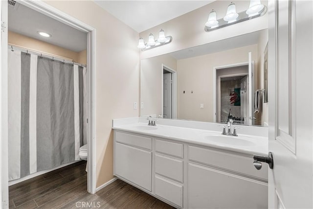 bathroom with wood finished floors, toilet, double vanity, and baseboards