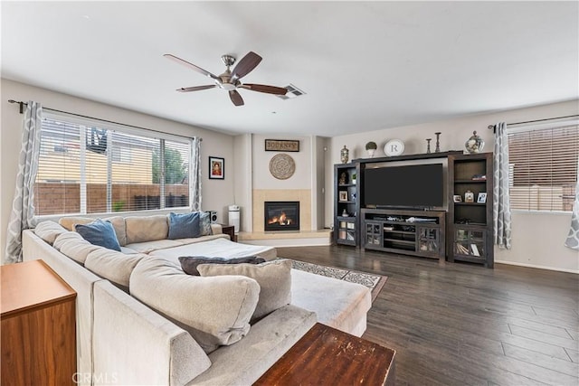 living area featuring ceiling fan, dark wood-style floors, a glass covered fireplace, and baseboards