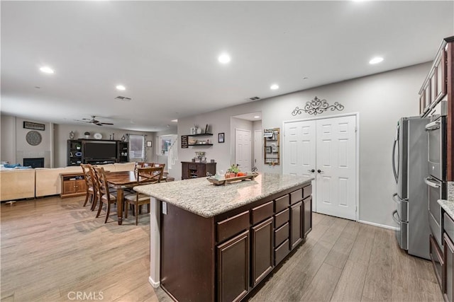 kitchen featuring ceiling fan, light wood-type flooring, dark brown cabinets, open floor plan, and a center island