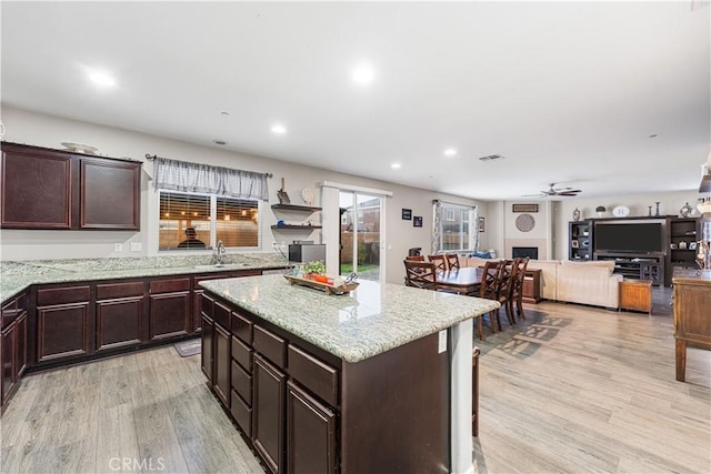 kitchen featuring a ceiling fan, light wood-type flooring, light stone counters, recessed lighting, and a center island