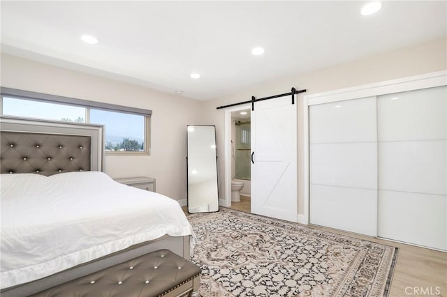bedroom with a barn door, recessed lighting, light wood-type flooring, ensuite bath, and a closet
