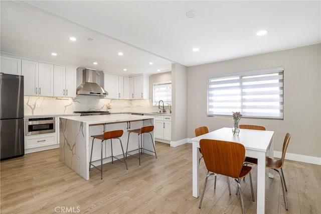 kitchen featuring wall chimney range hood, appliances with stainless steel finishes, a center island, a breakfast bar, and decorative backsplash