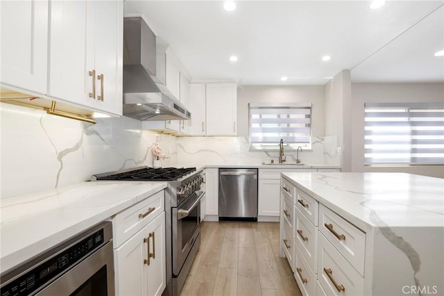 kitchen with stainless steel appliances, wall chimney range hood, a sink, decorative backsplash, and white cabinetry