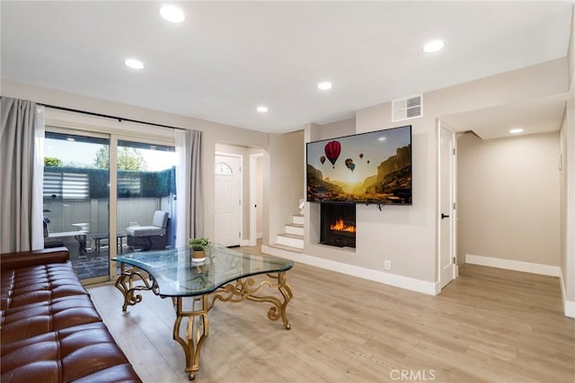 living room featuring baseboards, light wood finished floors, recessed lighting, and a warm lit fireplace