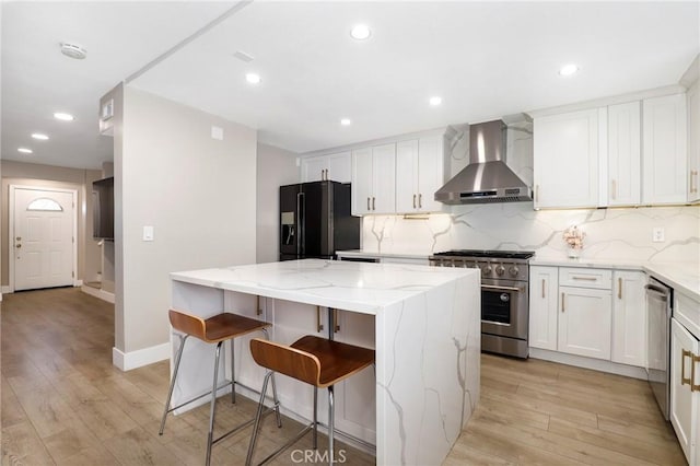 kitchen featuring wall chimney exhaust hood, appliances with stainless steel finishes, a center island, white cabinetry, and decorative backsplash