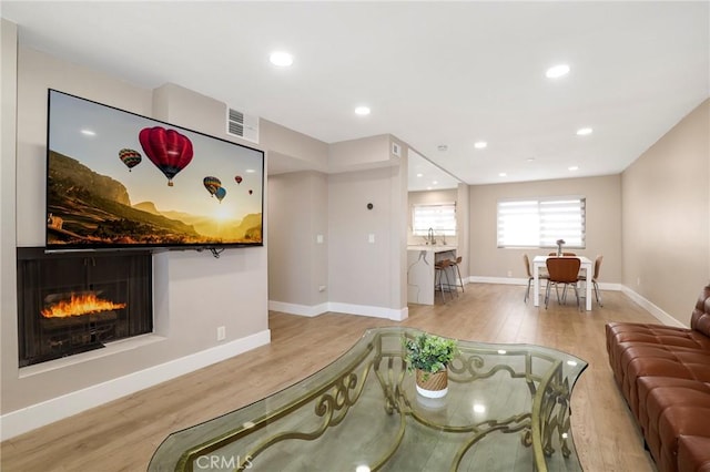 living room with wood finished floors, baseboards, a warm lit fireplace, and recessed lighting