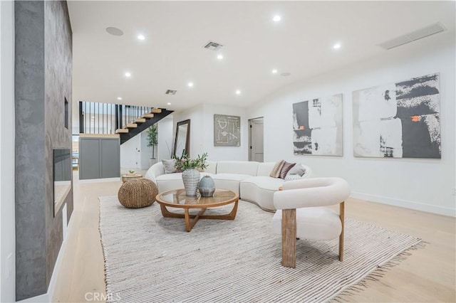living area featuring a premium fireplace, stairs, recessed lighting, light wood-style flooring, and baseboards