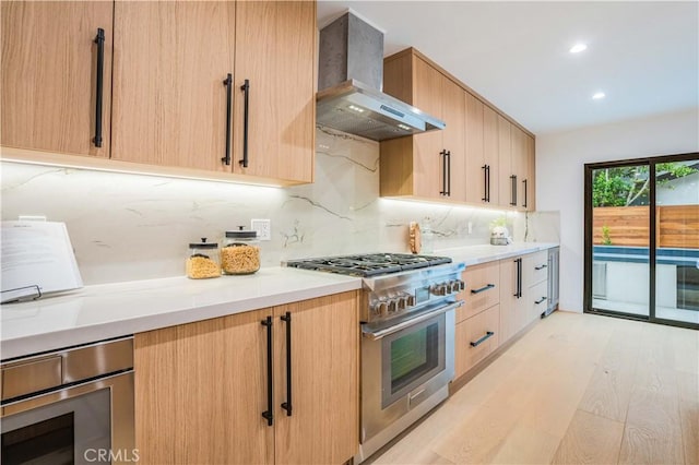 kitchen with high end stove, wall chimney range hood, light brown cabinetry, tasteful backsplash, and recessed lighting