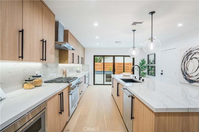 kitchen featuring a sink, wall chimney range hood, appliances with stainless steel finishes, modern cabinets, and light wood finished floors