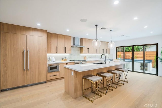kitchen with a sink, wall chimney exhaust hood, stainless steel gas stovetop, a breakfast bar area, and a center island with sink