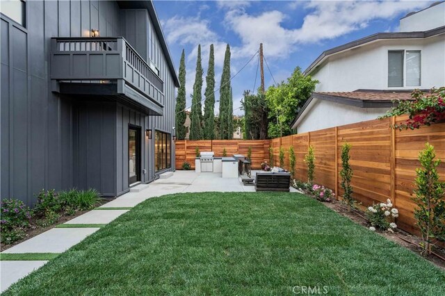 view of yard featuring a balcony, a patio, and exterior kitchen