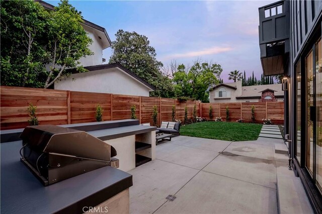 patio terrace at dusk with a fenced backyard and grilling area