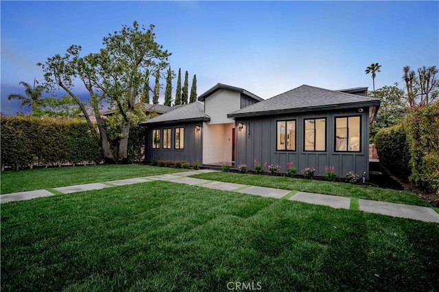 view of front facade featuring board and batten siding, a front yard, and roof with shingles