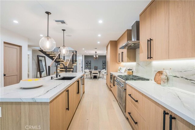 kitchen with a sink, wall chimney exhaust hood, stainless steel range, light wood-type flooring, and light brown cabinets