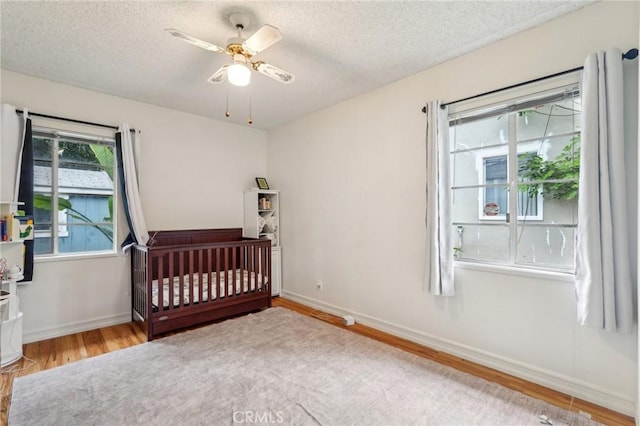 16133 Haldane St, Whittier, CA 90603 - bedroom with wood finished floors, a textured ceiling, baseboards, a crib, and a ceiling fan
