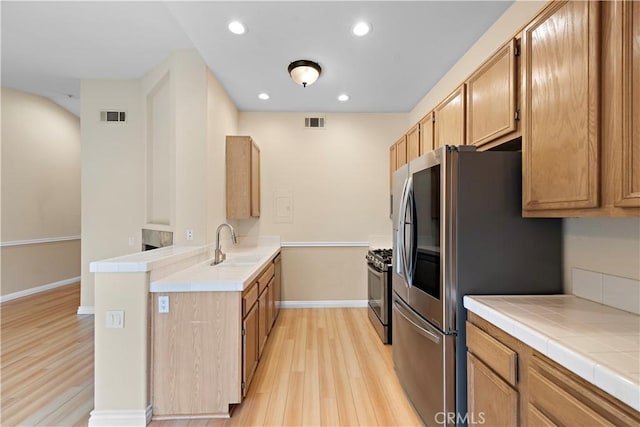 kitchen featuring light wood-style flooring, appliances with stainless steel finishes, a peninsula, baseboards, and tile countertops
