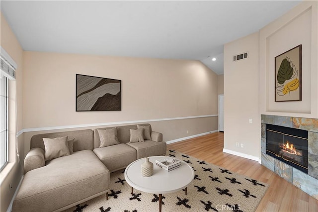 living area featuring wood finished floors, vaulted ceiling, a tile fireplace, and baseboards