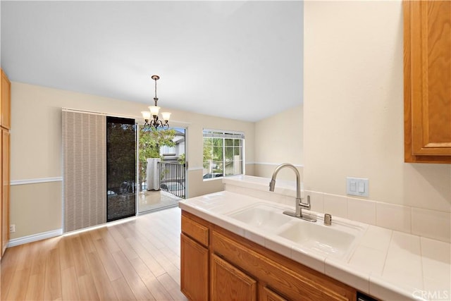 kitchen with a sink, tile countertops, light wood-type flooring, and brown cabinets