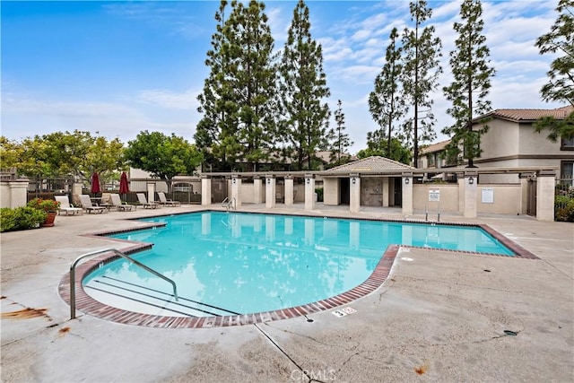 community pool with a patio, fence, and exterior kitchen