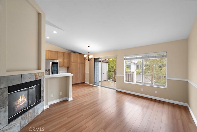 unfurnished living room featuring a chandelier, baseboards, light wood-type flooring, a tiled fireplace, and lofted ceiling