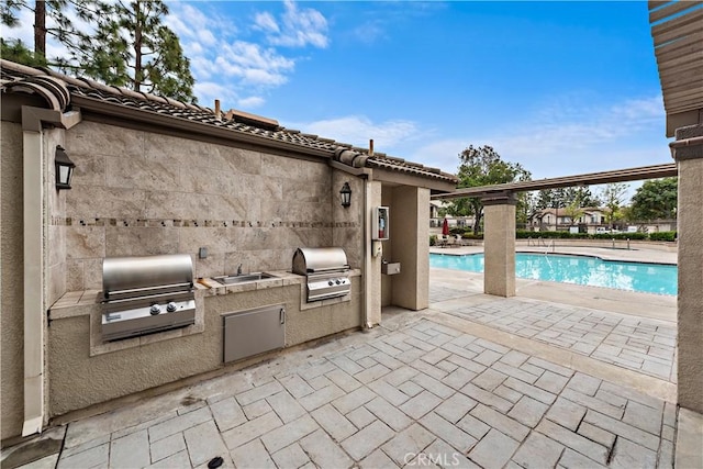 community pool with area for grilling, a grill, a patio area, and a sink