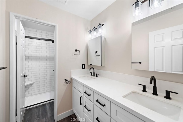 bathroom with tiled shower, double vanity, wood finished floors, and baseboards