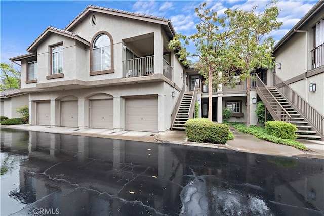 multi unit property featuring stairs, stucco siding, an attached garage, and driveway