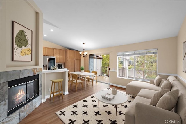 living area with vaulted ceiling, light wood-style floors, a chandelier, a fireplace, and baseboards