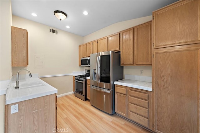 kitchen featuring appliances with stainless steel finishes, a sink, light wood finished floors, tile countertops, and recessed lighting
