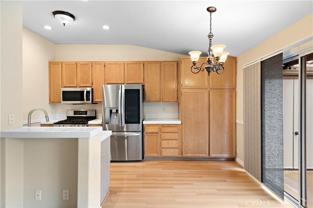 kitchen with stainless steel appliances, tile countertops, a chandelier, light wood finished floors, and pendant lighting