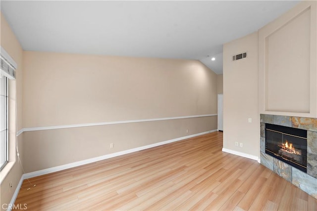 unfurnished living room featuring a tiled fireplace, wood finished floors, lofted ceiling, and baseboards