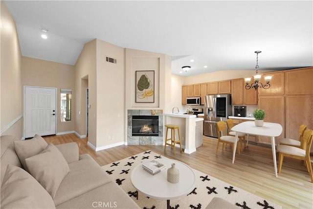 living area with vaulted ceiling, light wood-style flooring, a chandelier, baseboards, and a fireplace