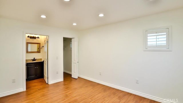 unfurnished bedroom with light wood finished floors, recessed lighting, ensuite bath, baseboards, and a spacious closet
