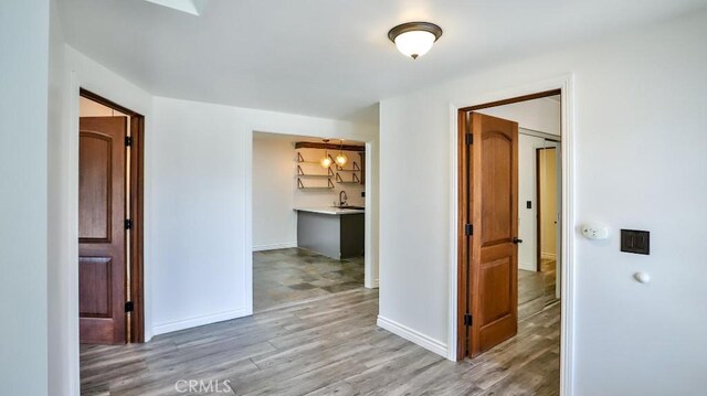 hallway with light wood-style floors, baseboards, and a sink