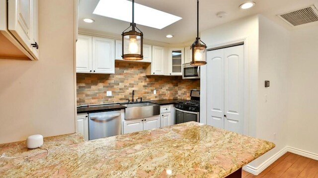 kitchen with stainless steel appliances, tasteful backsplash, white cabinetry, a sink, and light wood-type flooring
