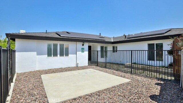 back of house with stucco siding, a patio area, and roof mounted solar panels