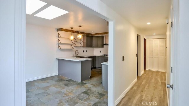 kitchen featuring a peninsula, baseboards, light countertops, hanging light fixtures, and a sink