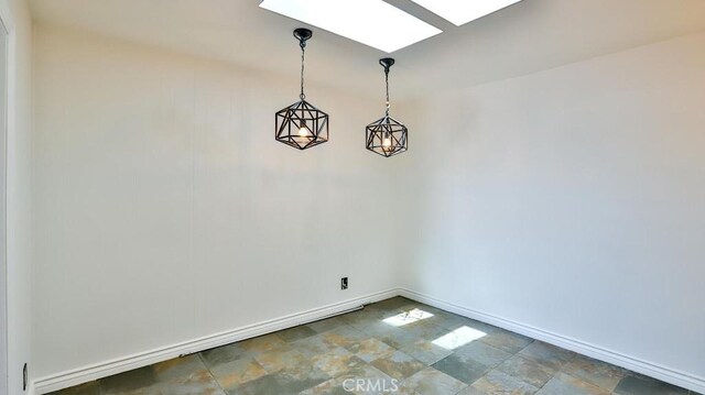 unfurnished dining area featuring stone finish flooring, a skylight, and baseboards