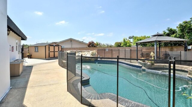 view of swimming pool featuring a storage unit, a gazebo, a fenced backyard, and an outbuilding