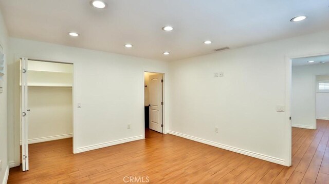 unfurnished bedroom with light wood finished floors, a walk in closet, recessed lighting, baseboards, and a closet