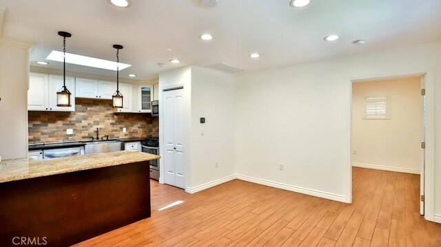kitchen with backsplash, white cabinetry, baseboards, decorative light fixtures, and light wood finished floors