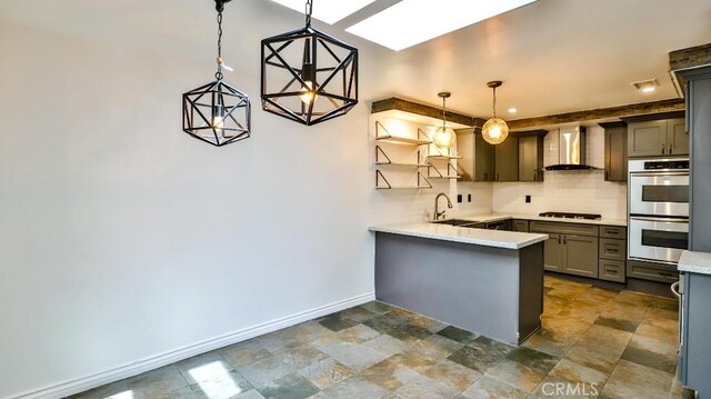 kitchen with wall chimney range hood, double oven, gas stovetop, tasteful backsplash, and baseboards