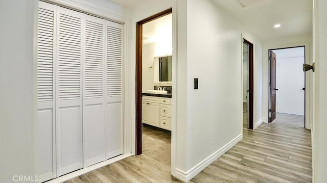 corridor with a sink, light wood finished floors, recessed lighting, and baseboards