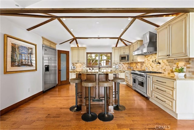 4117 Vanetta Pl, Studio City, CA 91604 - kitchen featuring wall chimney exhaust hood, built in appliances, cream cabinets, a kitchen breakfast bar, and light stone countertops